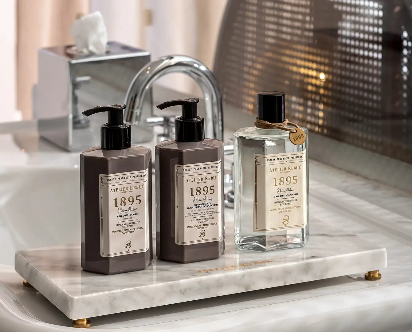 Set de trei produse de baie Atelier Rebul 1895 în nuanțe mate maro și sticle de sticlă transparentă cu dozatoare cu pompă neagră.