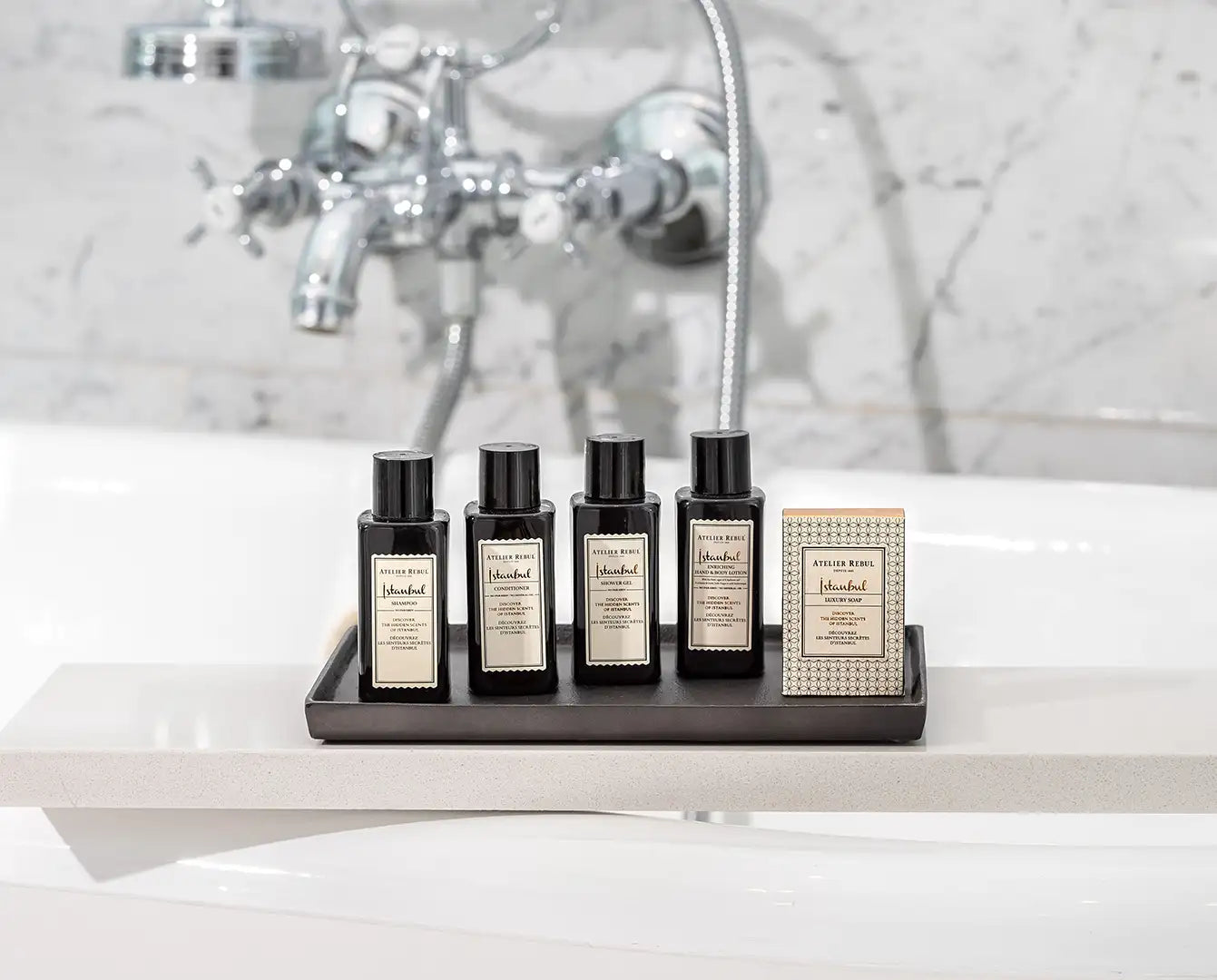 Set de patru sticle negre din sticlă cu etichete de culoare crem și un săpun de baie dreptunghiular asortat, toate de la atelier rive.