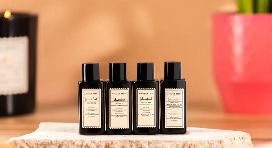 Patru sticle de sticlă neagră cu etichete albe, fiecare conținând un produs diferit atelier reine.